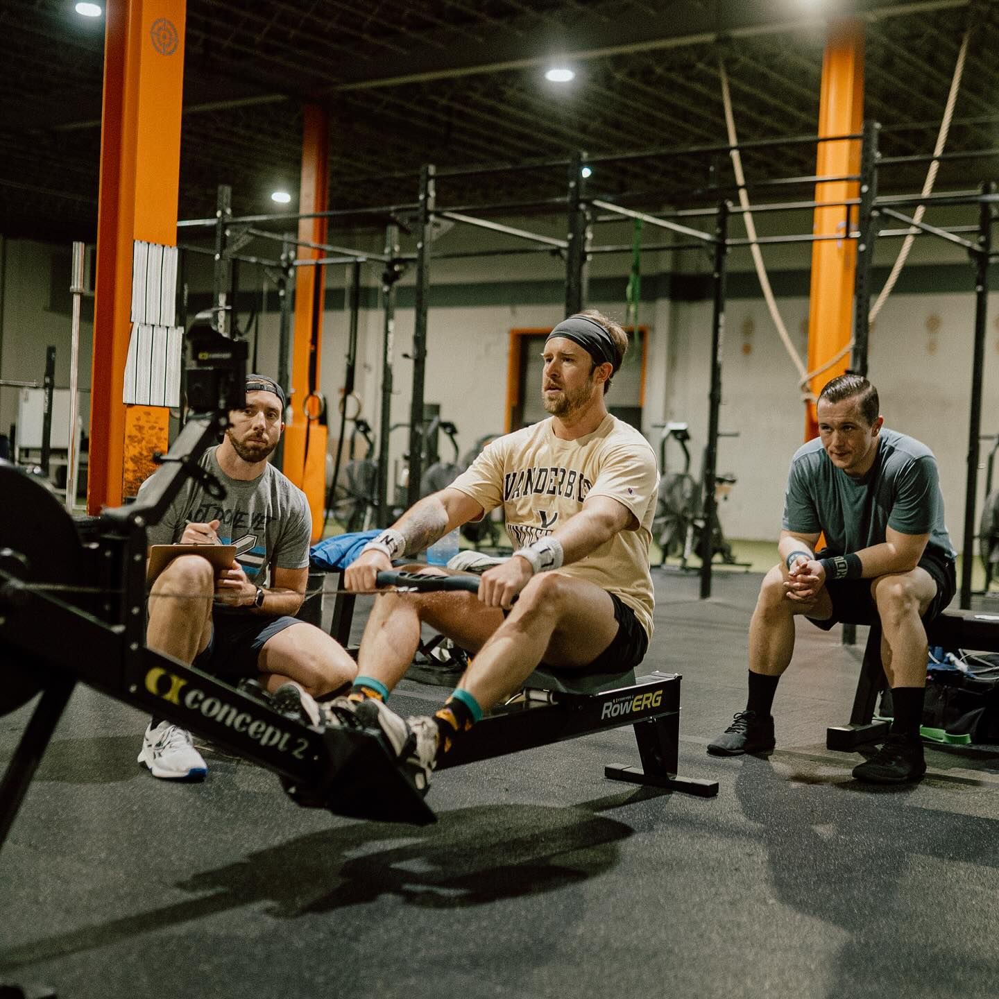 Three men are sitting on rowing machines in a gym.