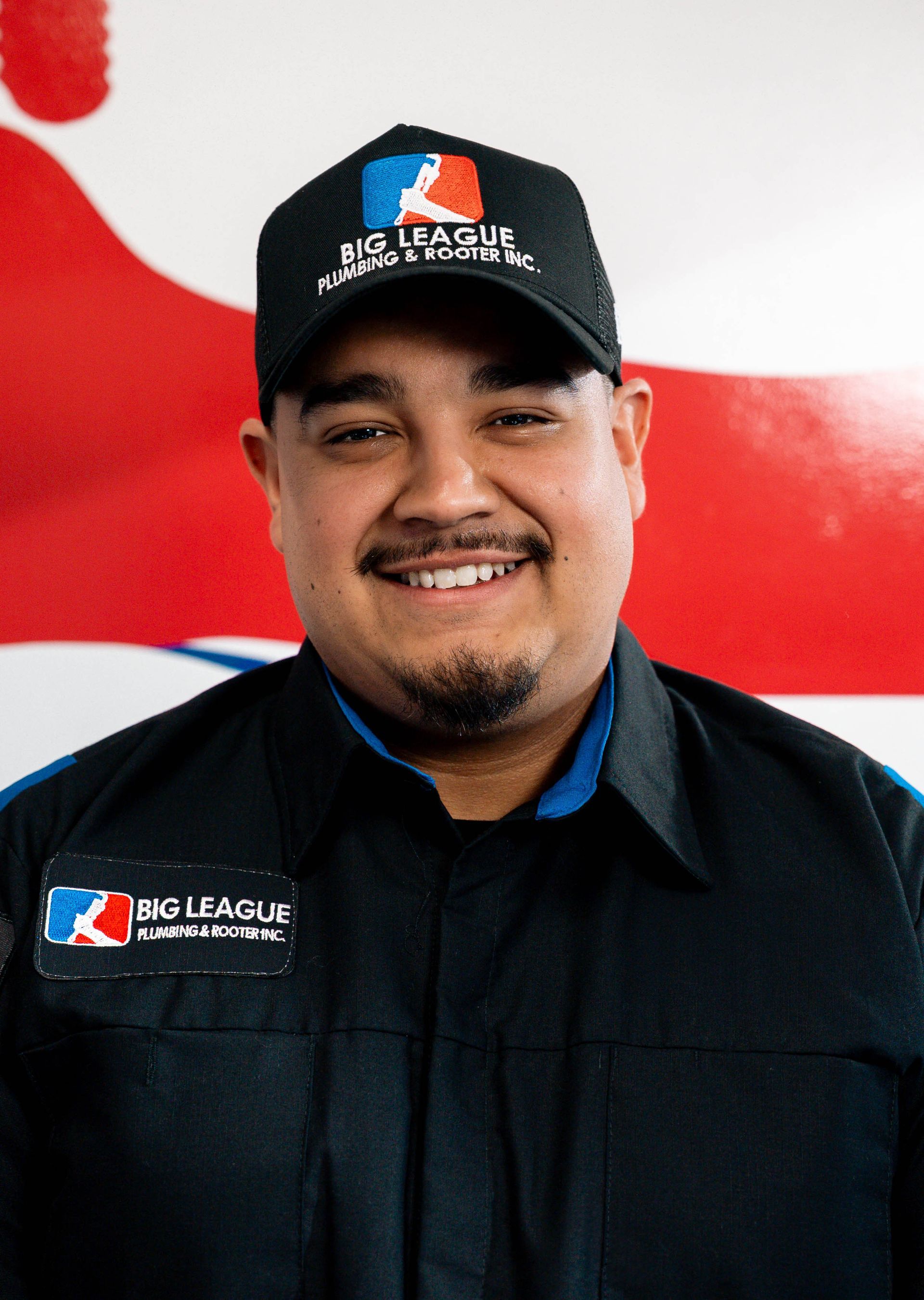 Smiling employee in black uniform and cap standing before a red-and-white BC Eagle backdrop