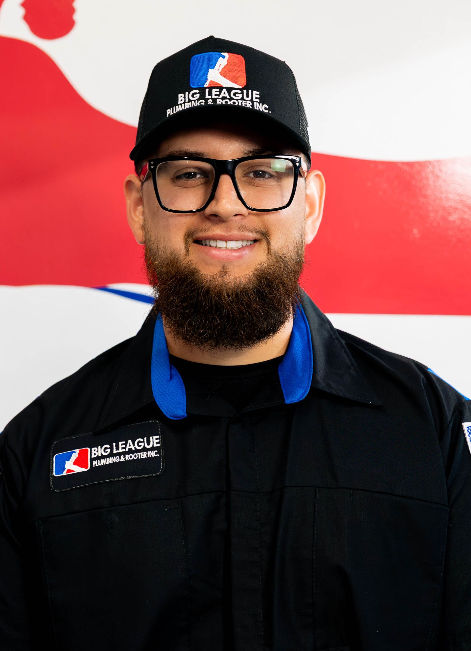Man in black uniform and cap smiling in front of a red-and-white wall