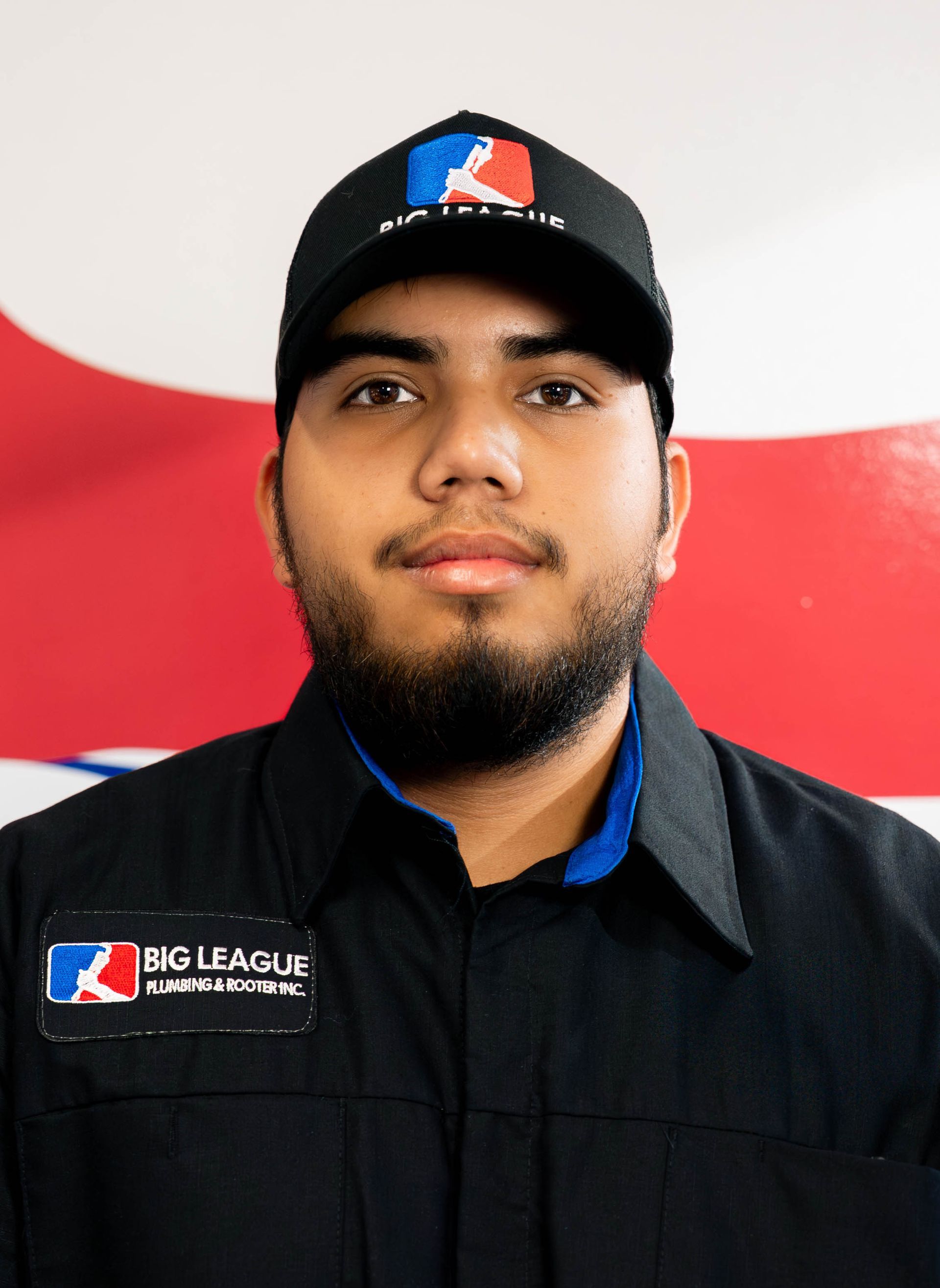 Portrait of a uniformed Big League umpire wearing a black cap, standing against a red and white background