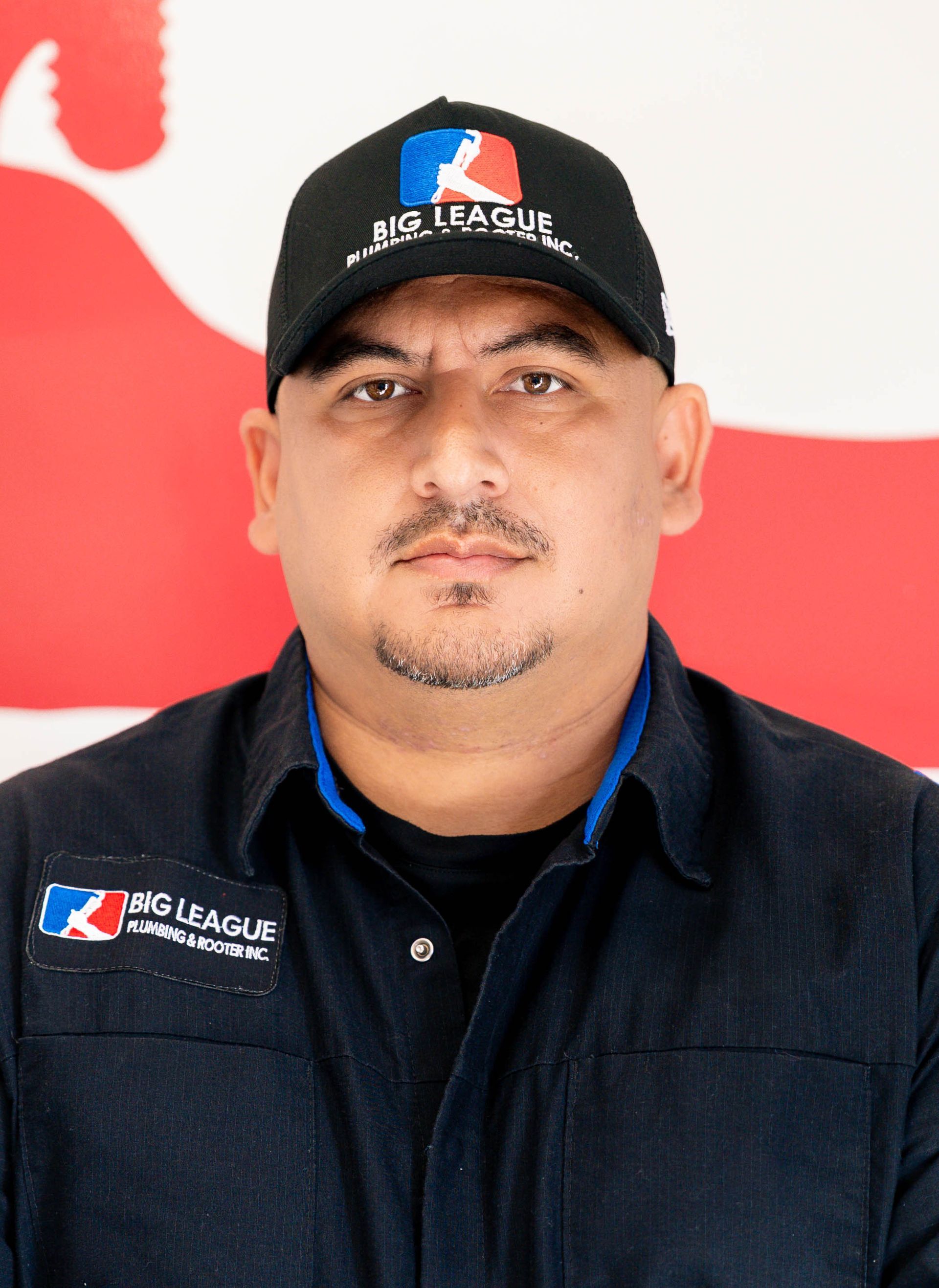 Man in black cap and shirt with Red League logo, standing against a red-and-white background