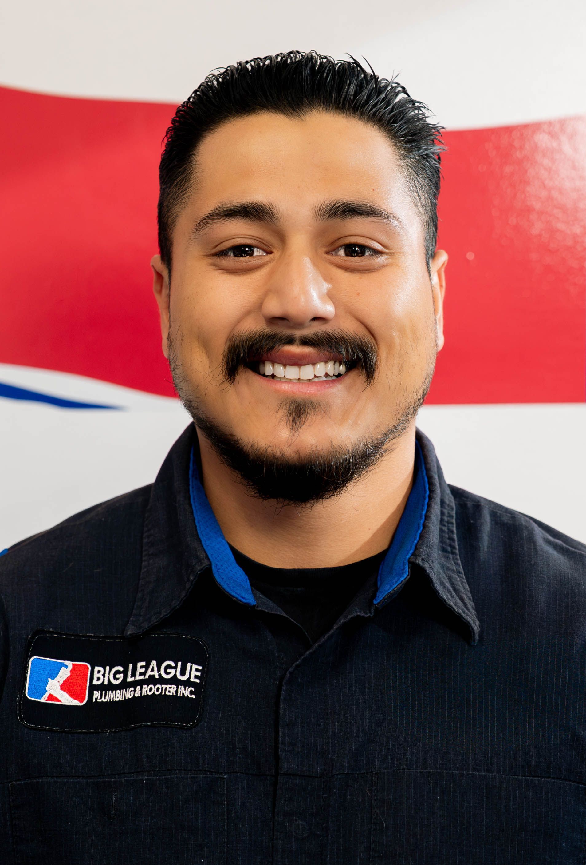 Smiling man in black jacket with a league logo, standing before a red and white background