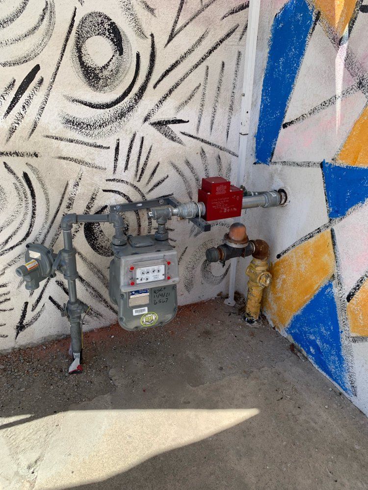 Gas meter and pipes on a wall with black, white, blue, and yellow geometric mural.