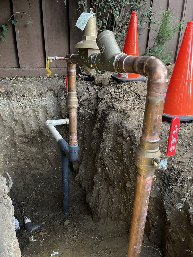 Trenched copper and PVC pipes beside a house, marked by orange safety cones.