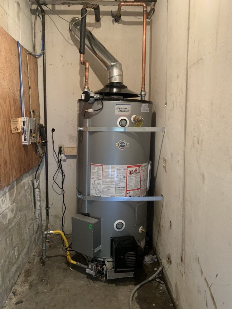 Large gray water heater with vent pipes in a narrow utility closet between unfinished walls.
