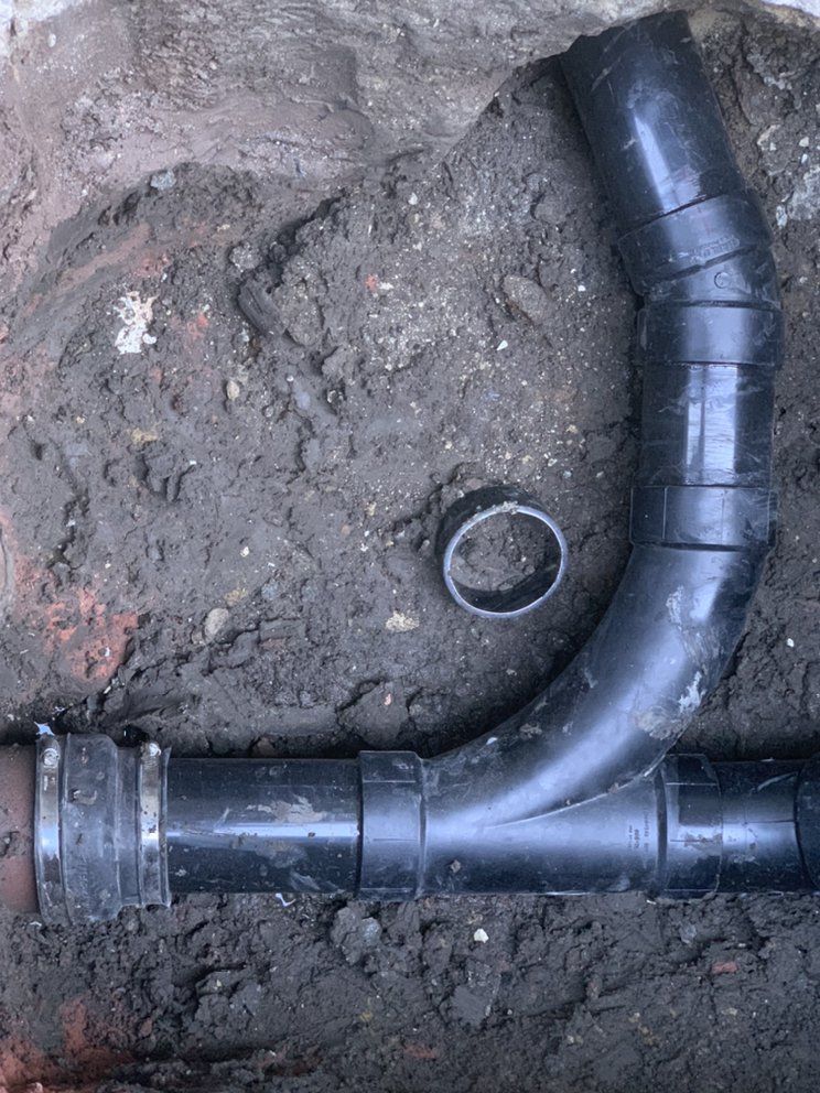 Black plastic drain pipe elbow in muddy ground with a small round fitting nearby