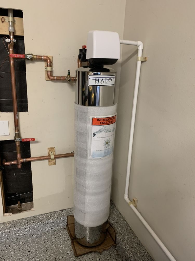 Water heater wrapped in insulation, with copper pipes, in a utility room corner.