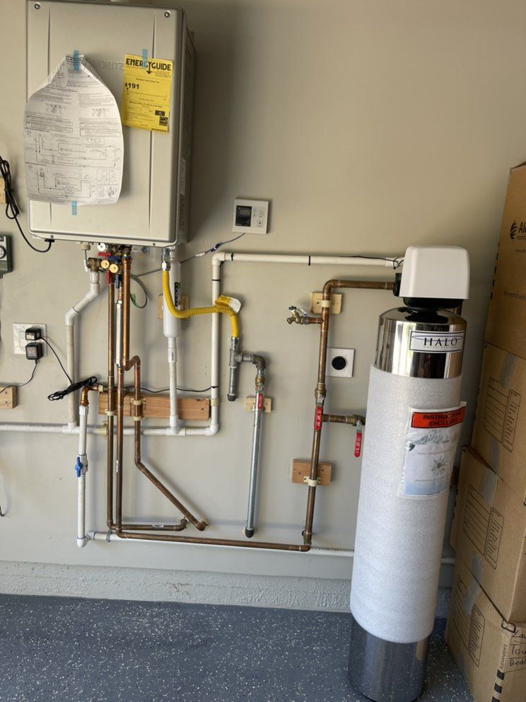 Water heater and utility equipment in a small mechanical room with pipes and valves on a wall.