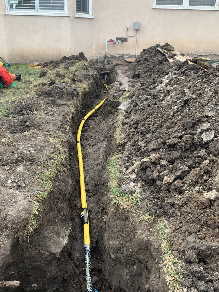 Backyard trench with a yellow gas line laid beside a house foundation