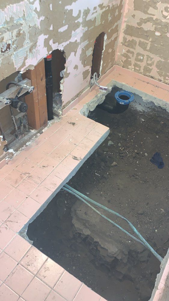 Bathroom under renovation with exposed wall studs, tile floor, and an open shower pit.