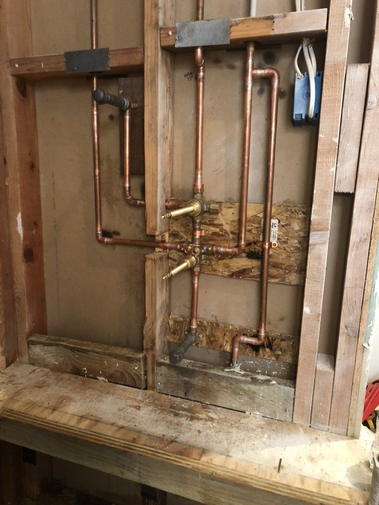 Exposed copper pipes and brass valves inside a wall cavity during plumbing work