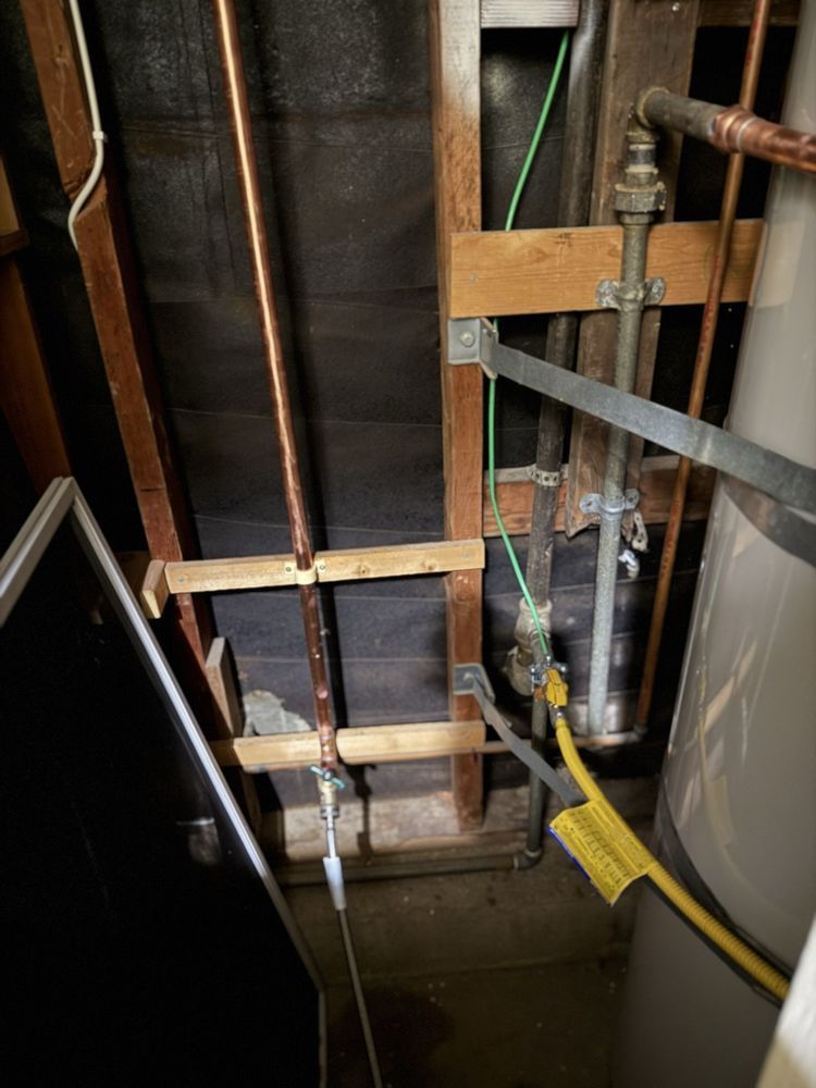 Exposed wall framing with copper pipes, valves, and yellow hose in a utility space