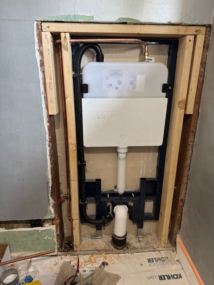 Exposed wall-mounted toilet cistern in unfinished bathroom wall framing