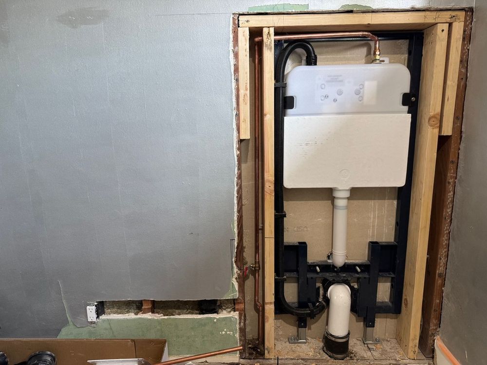 Open wall with exposed white plumbing fixture and pipes in a bathroom alcove.