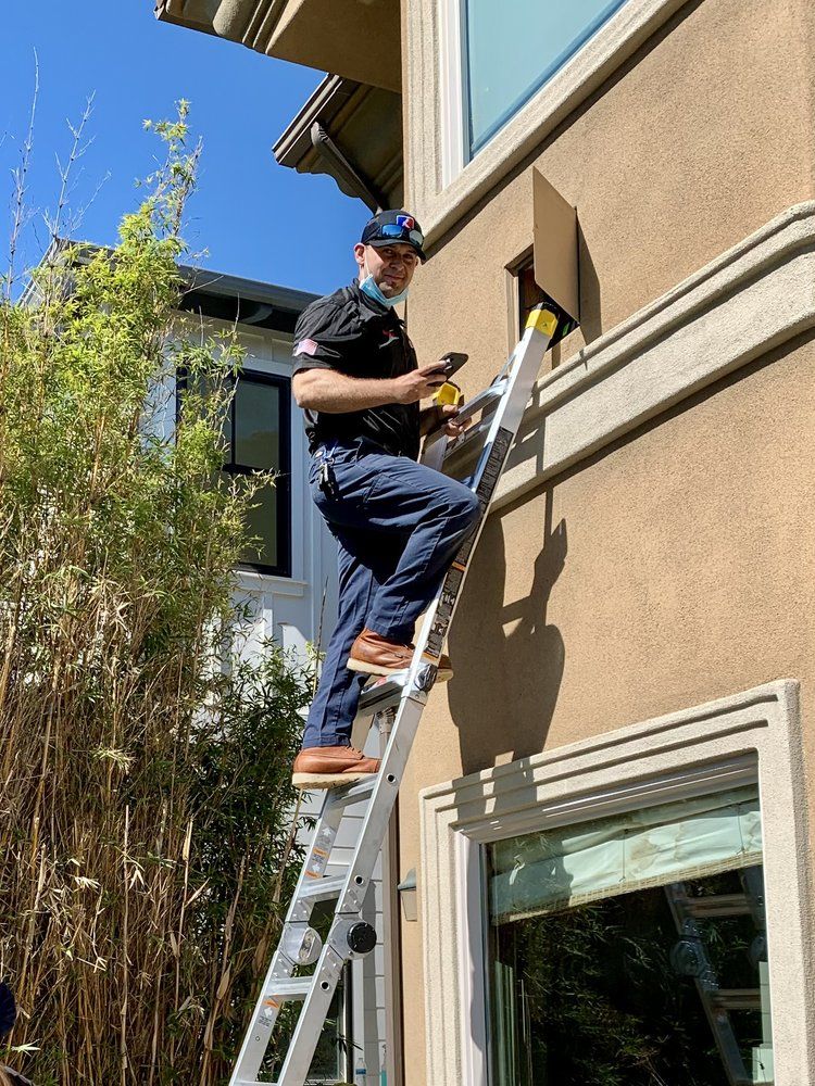 Worker on ladder painting exterior wall of a house beside a window.