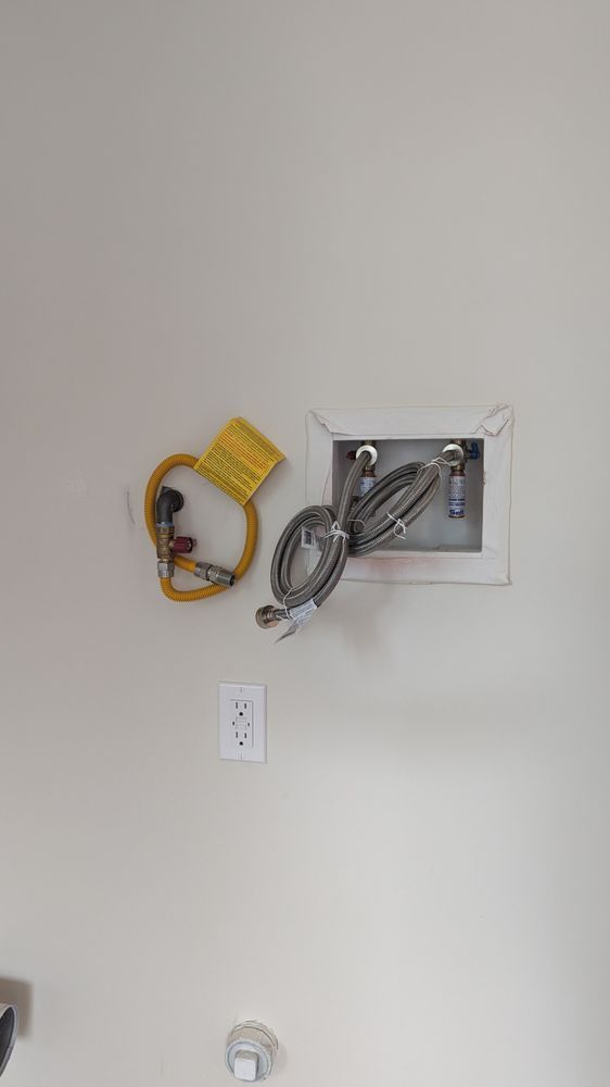 Wall with exposed plumbing, coiled hose, and electrical outlets in a plain room