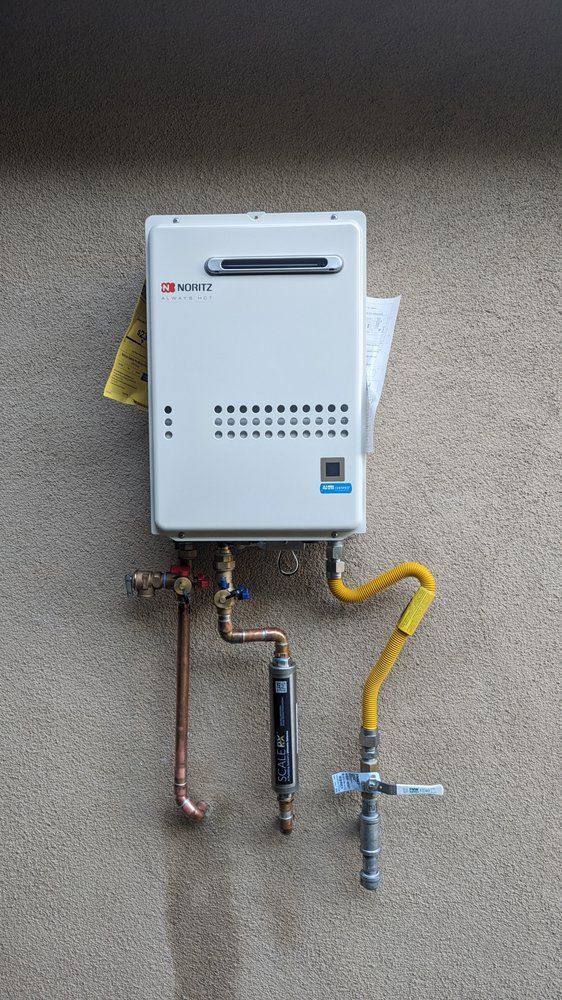 Wall-mounted gas water heater with exposed copper and yellow piping against a gray wall.