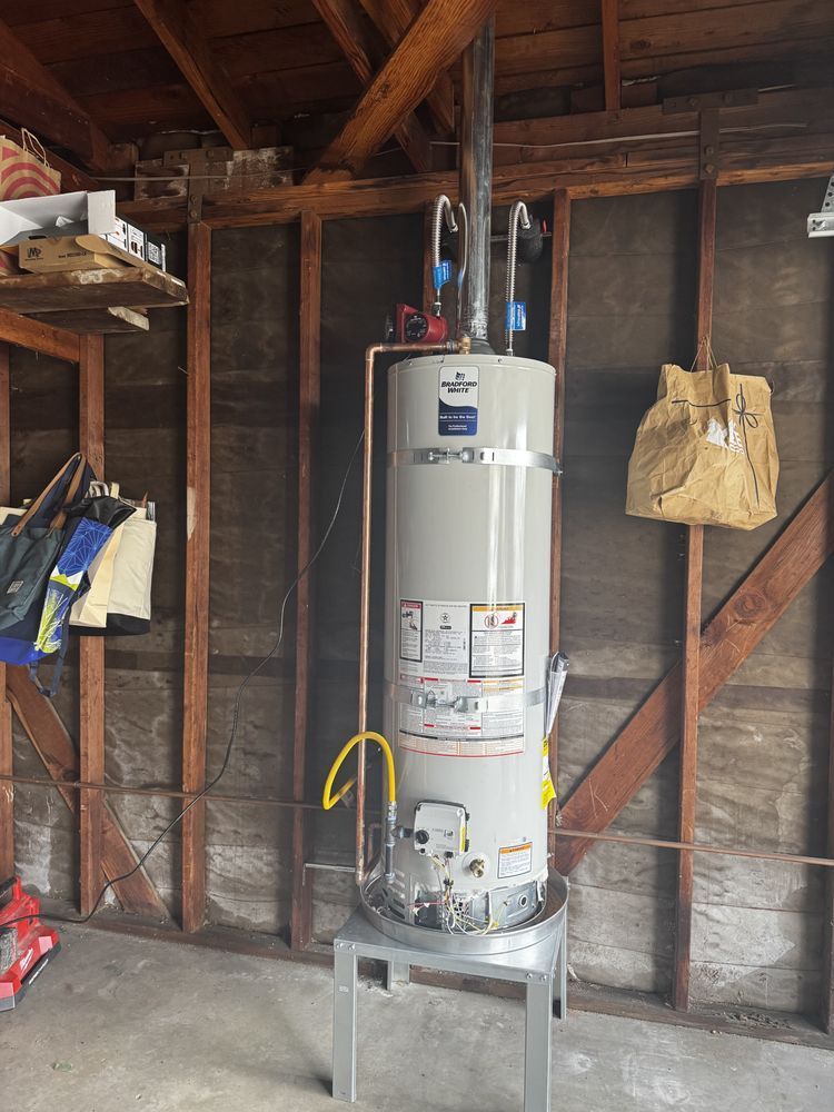 Water heater in an unfinished garage, mounted on a metal stand against exposed wooden wall framing.