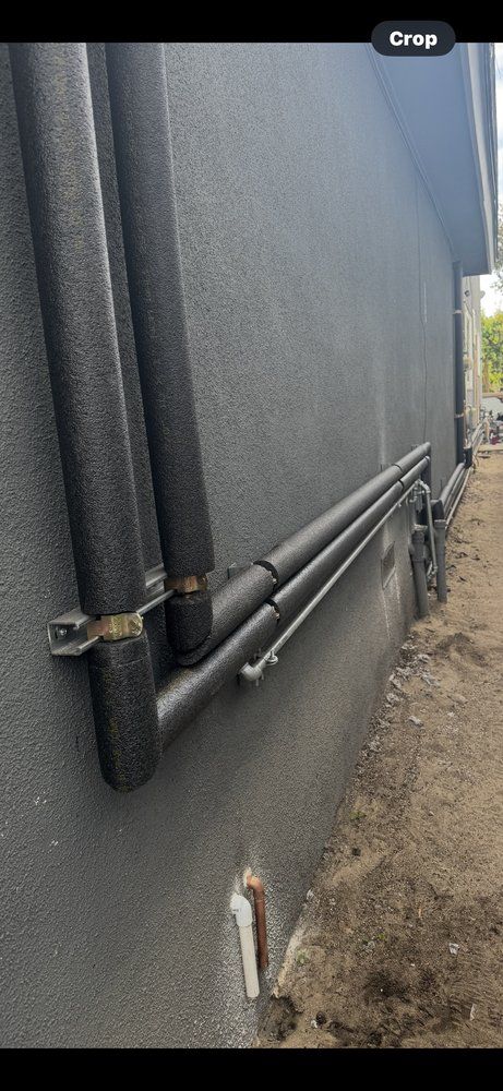 Black corrugated building wall with exposed pipes along a gravel walkway outdoors