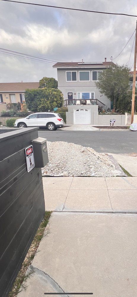 Residential street view with gravel driveway, white house, parked SUV, and cloudy sky