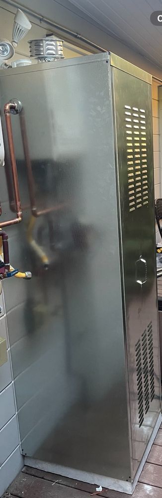 Tall silver metal cabinet in an industrial room, with copper tubing and vents on the side.