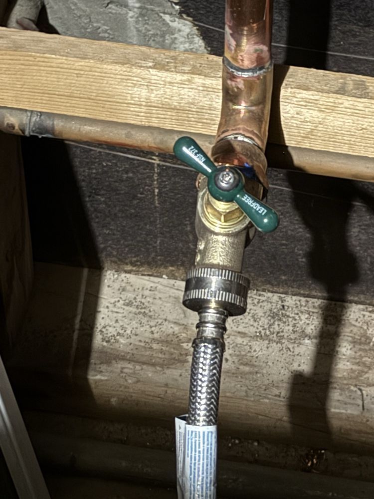 Close-up of a green-handled outdoor water valve connected to a hose and copper pipe.
