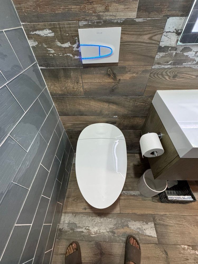 Small bathroom with toilet, sink, toilet paper holder, and blue flush button on tiled wall.