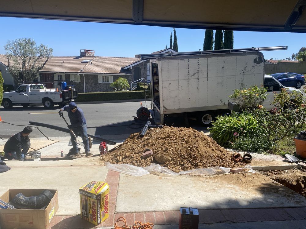 Workers shoveling dirt beside a white dump truck at a residential street construction site