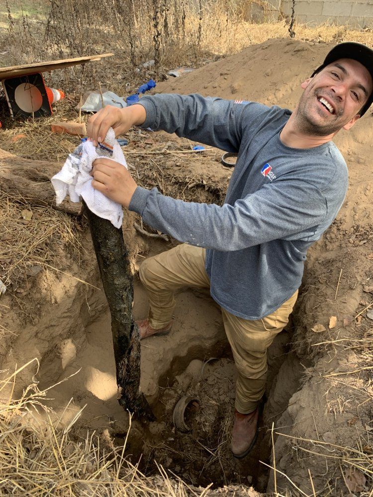 Smiling worker standing in a trench, wiping hands with a cloth at a construction site
