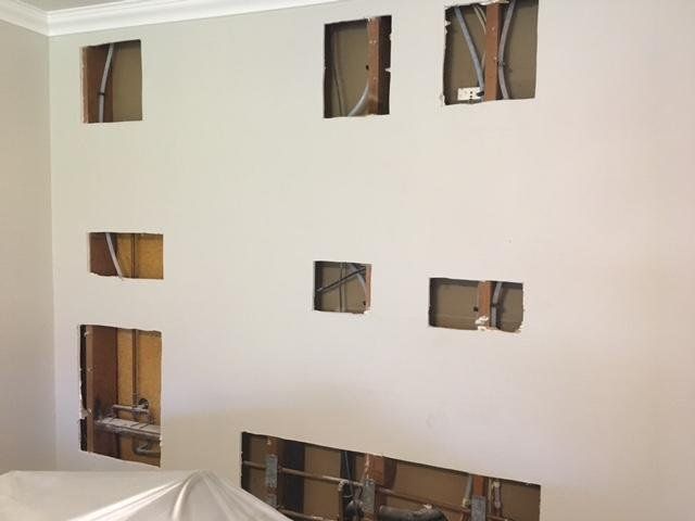 Wall with several rectangular cutouts exposing wiring and studs inside a room under renovation