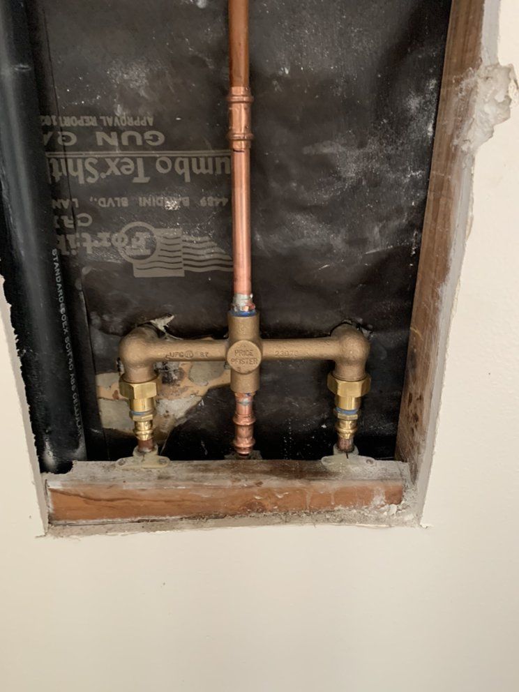 Copper plumbing pipes and brass valves inside a wall cavity with exposed insulation and drywall edges