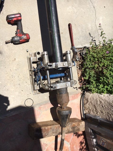 Power drill attached to a pipe tool on concrete, with a red-handled lever and a drill nearby.