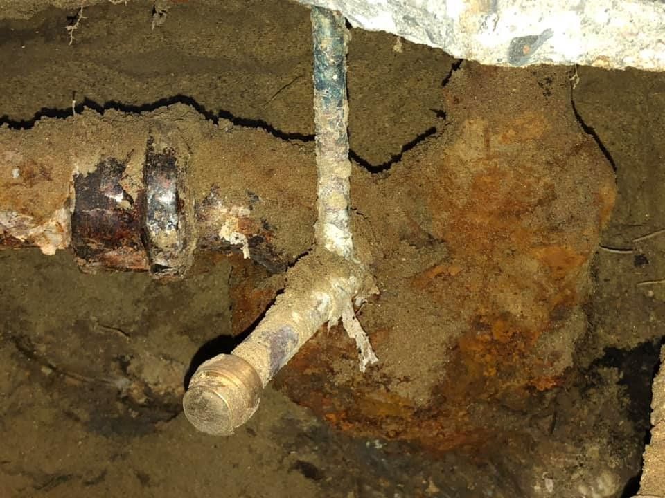 Exposed rusty metal pipe in cracked soil against a rough dirt wall