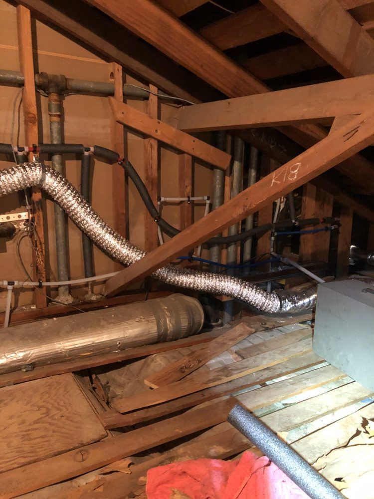 Attic with exposed wooden beams, metal ventilation ducts, and insulation on the floor.