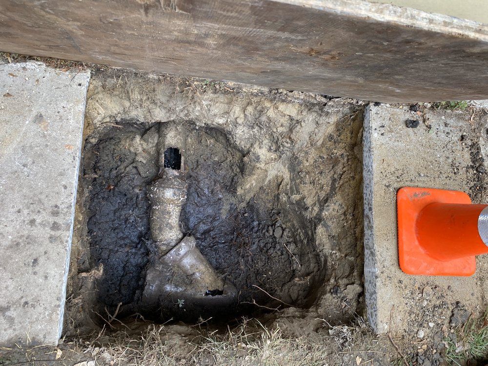 Small gray metal valve in a concrete opening beside an orange pipe cap or marker