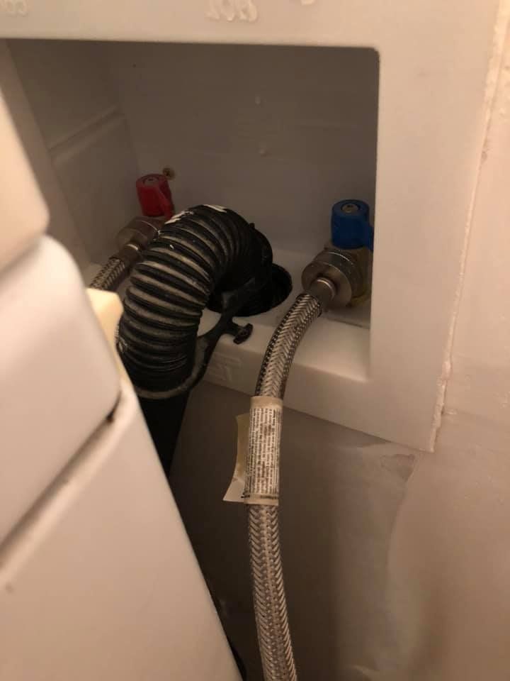 Laundry hookup in a wall niche with black and silver hoses and blue and red valves