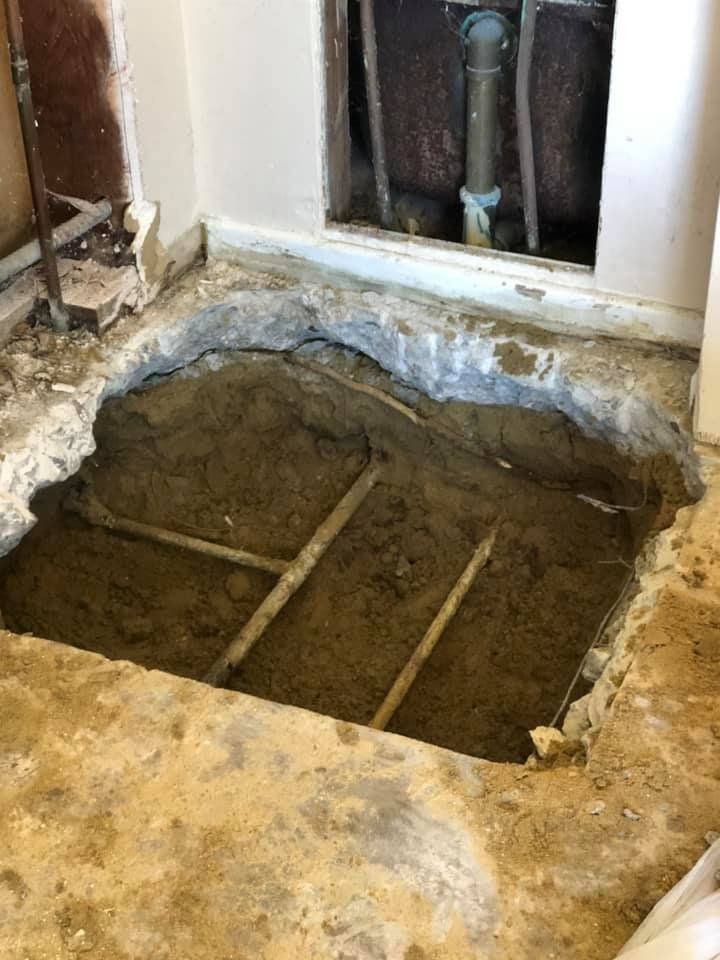 Open floor hole with exposed dirt and metal bars in a damaged room