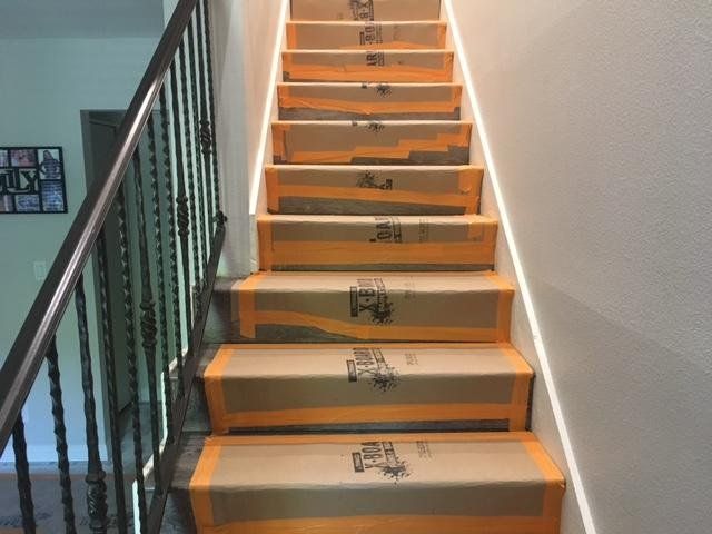 Indoor staircase with beige steps, orange edges, and a black railing beside a white wall.