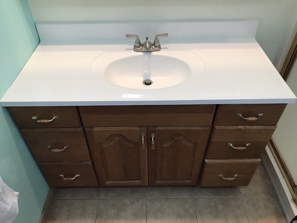 Bathroom vanity with white countertop, oval sink, and dark wood cabinets and drawers
