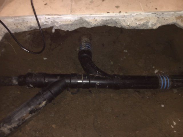 Black plastic pipes joined in a dirt trench under a concrete edge