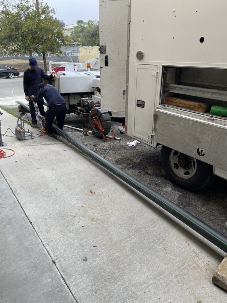 Workers moving long metal pipes beside a white truck at an outdoor construction site