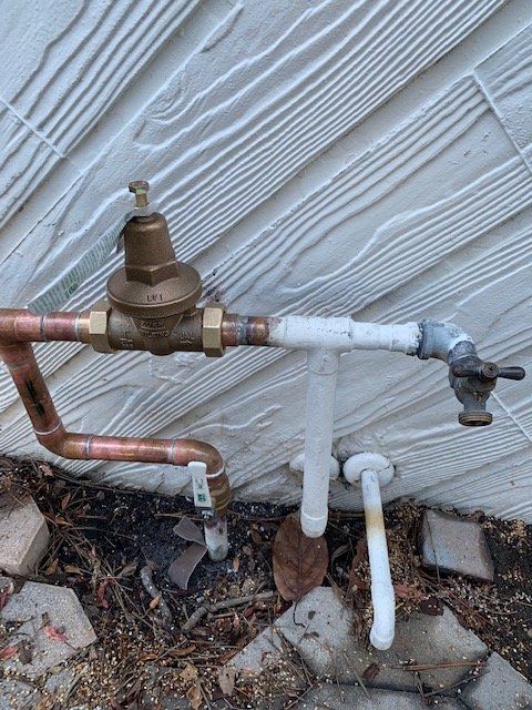 Outdoor water pressure regulator and pipes mounted on a house wall near the ground