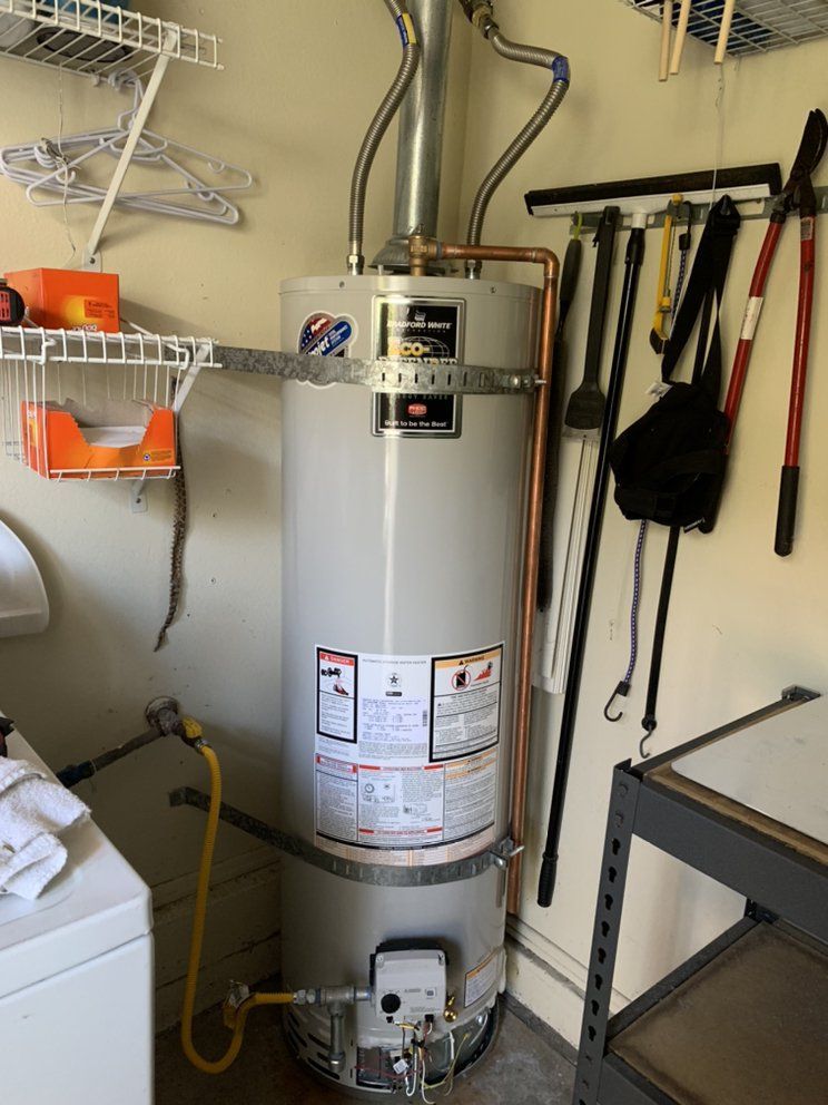 White water heater in a utility closet with shelves, hoses, and cleaning tools on the wall