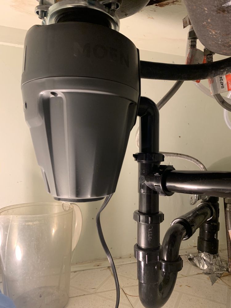 Grey water filtration unit under a sink with black pipes and a clear glass below it