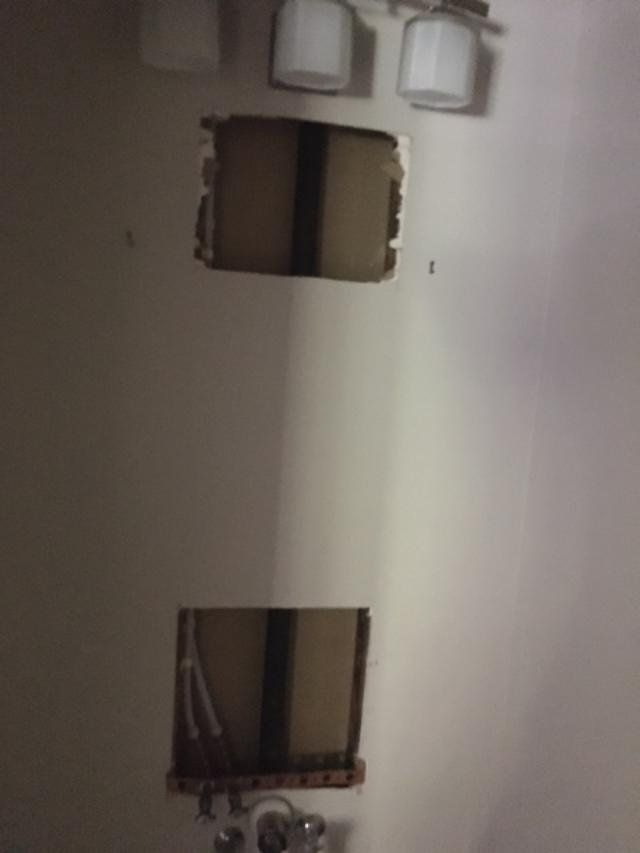 Interior wall with two square openings and a lower rectangular opening, showing exposed wiring and piping.