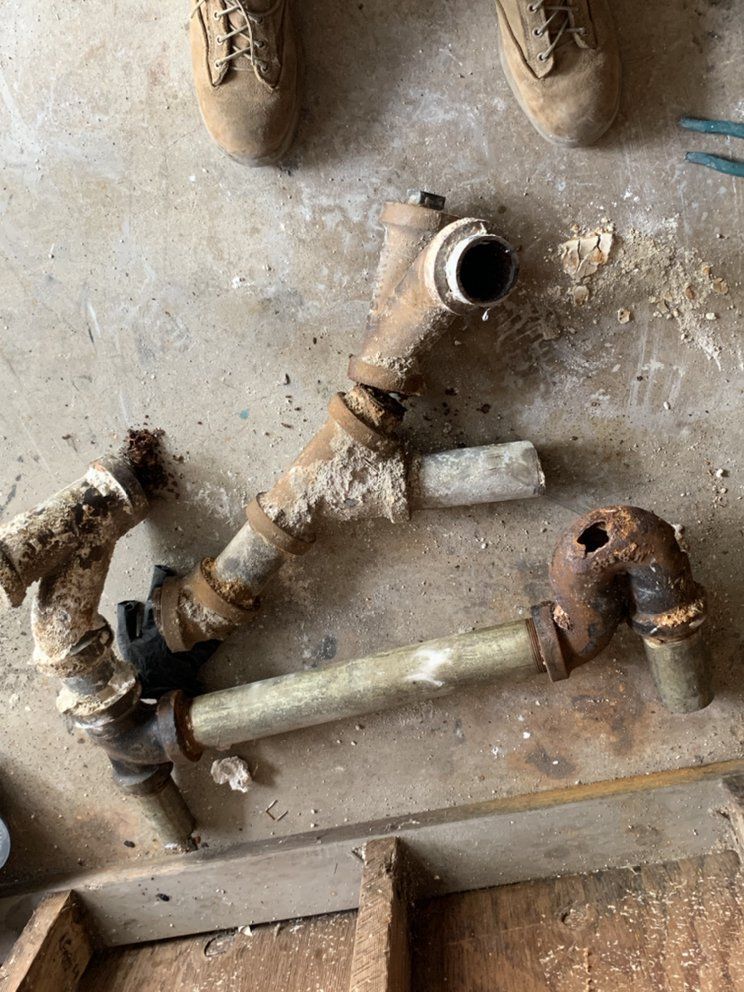 Old rusty metal pipes and valves against a concrete floor, with one open pipe end visible.