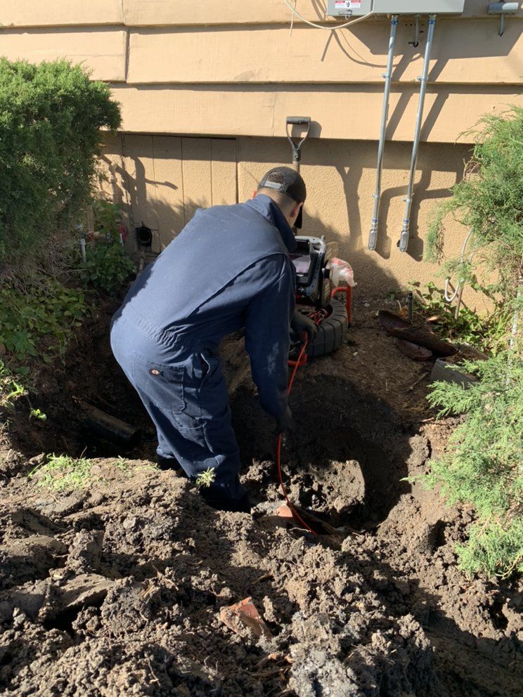 Worker using a trenching machine to dig soil in a garden beside a house