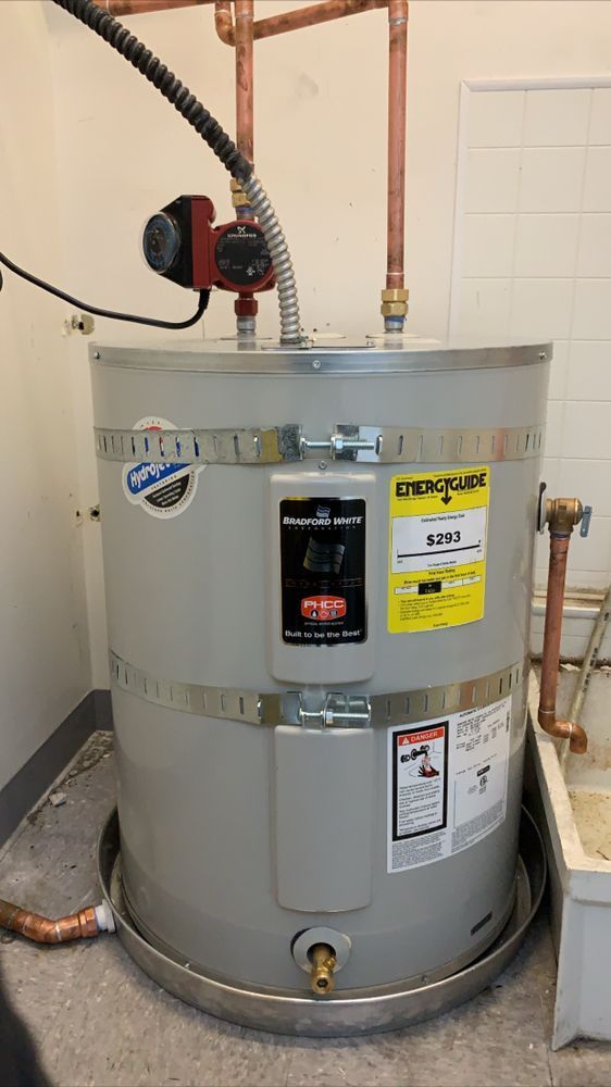 Grey water heater in a utility closet with copper pipes and warning labels.