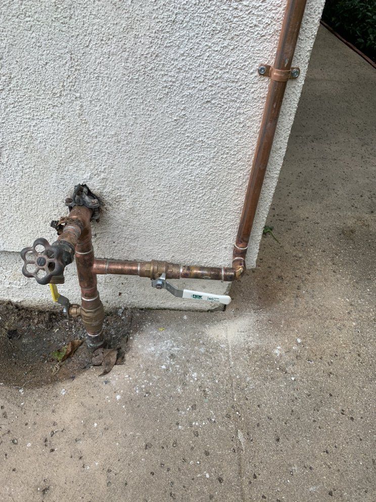 Rusty outdoor water valve and copper pipes against a stucco wall on a concrete floor