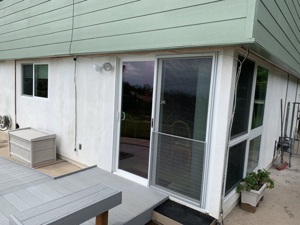Patio with sliding glass door, small deck, and potted plants beside a house